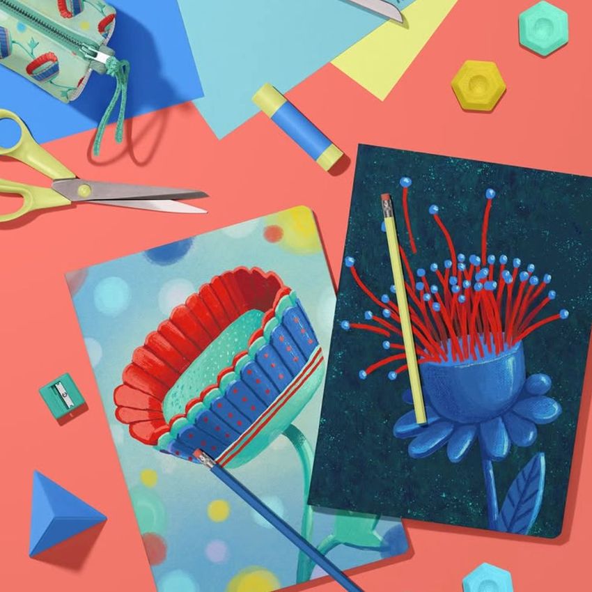 Stationery mockup featuring two A4 notebooks with colorful floral illustrations, pencils, scissors, and geometric props on a coral surface.