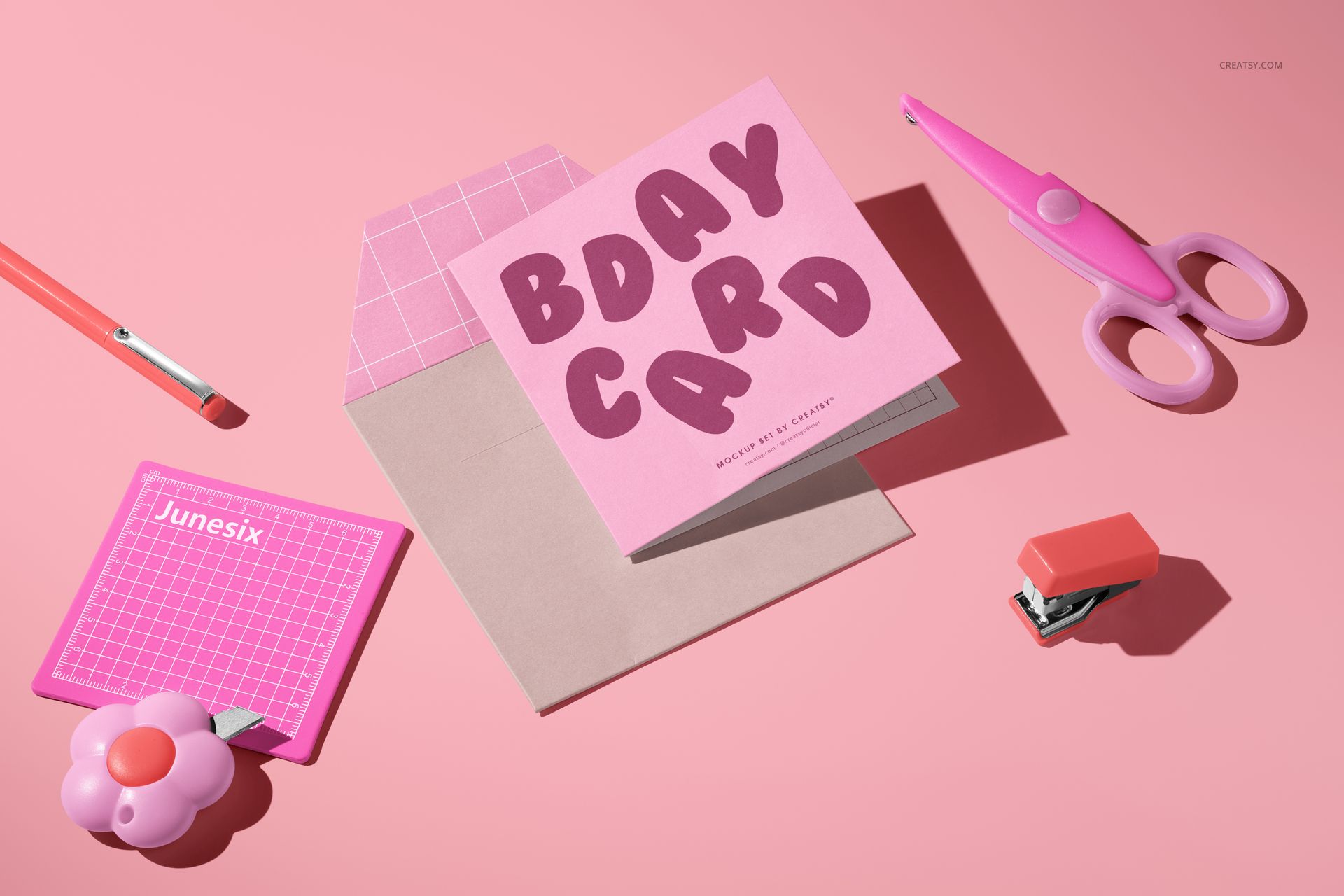 Small square greeting card mockup shown on a pink background with envelope, scissors, and stationery props.