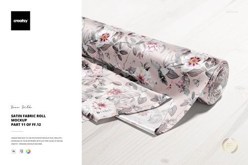 PSD mockup of a satin fabric roll with intricate floral designs in soft pink and gray tones, placed on a light wood table.