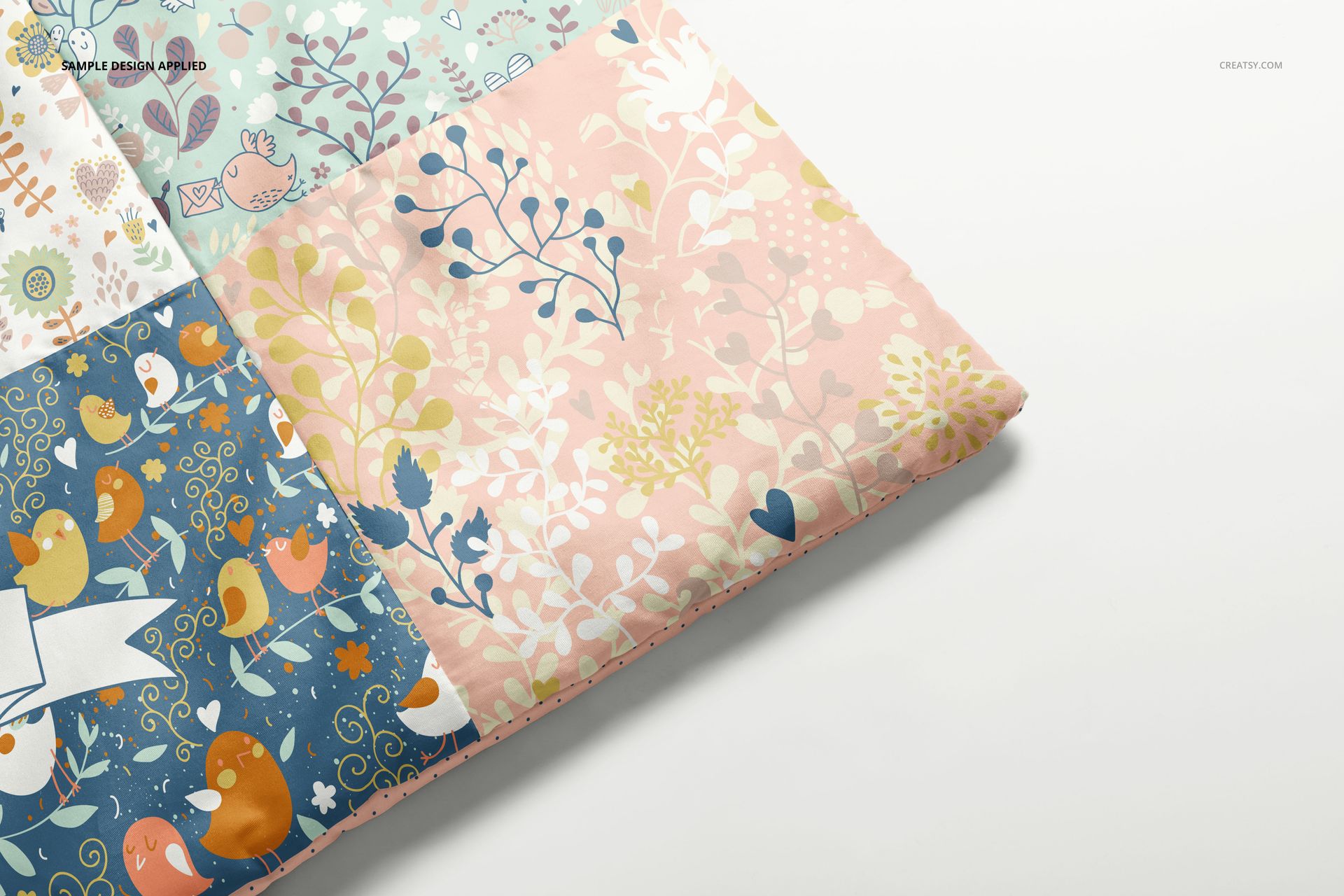 Front angled view of a baby patchwork quilt mockup showing colorful squares with whimsical nature and bird motifs.