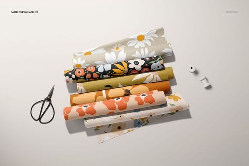 PSD mockup showing fabric rolls in floral prints, partially unrolled, with sewing tools arranged nearby.