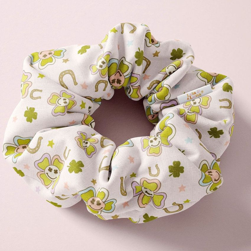 Hair scrunchie mockup featuring a white fabric with green clover, horseshoe, and star patterns on a light pink background.