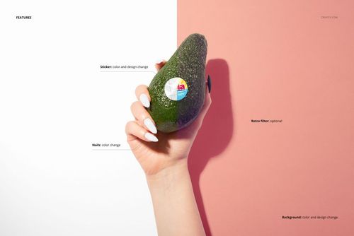 Hand holding a whole avocado with a round sticker on its surface, set against a split pink and white background.