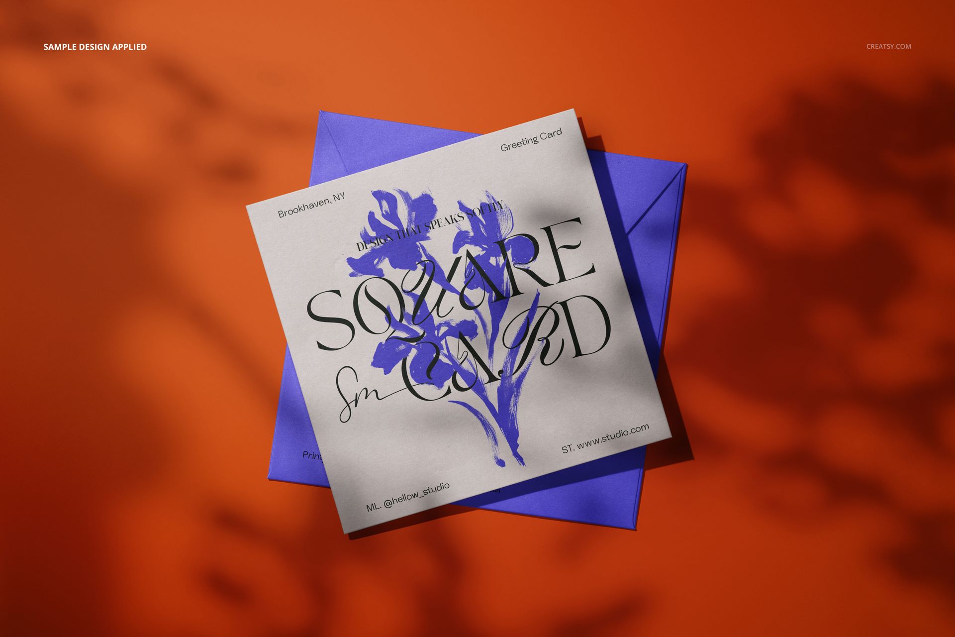 Square greeting card mockup featuring a floral design on a white card, placed over a blue envelope on an orange surface.
