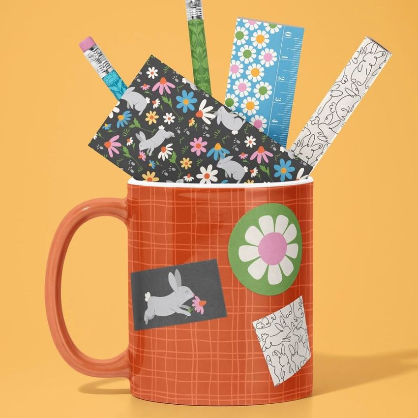 Mug mockup with a red checkered pattern holds pencils, a ruler, and stationery decorated with bunny and floral designs on a yellow background.