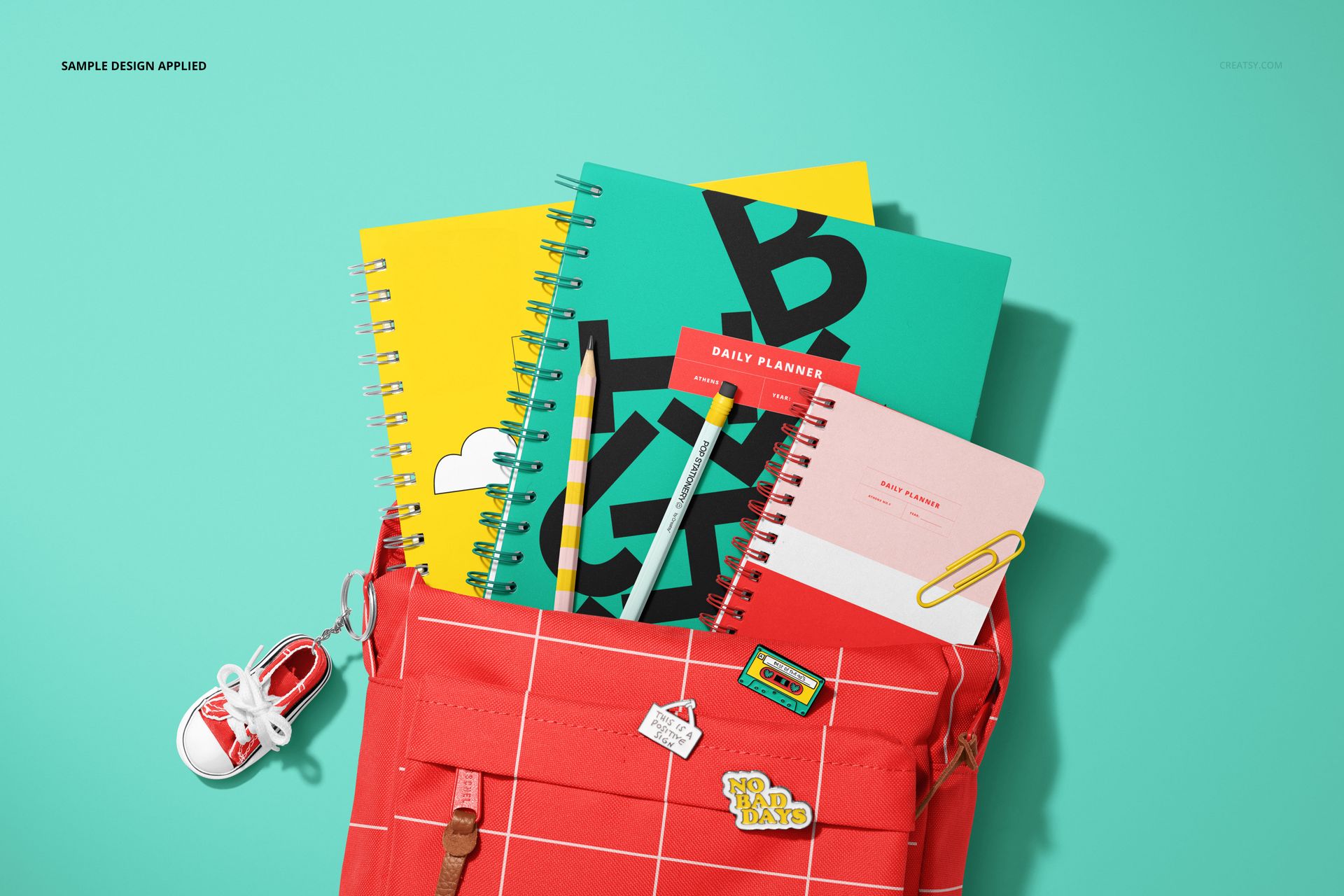 PSD mockup showing a school backpack with pins and keychain, containing spiral notebooks in vibrant colors.