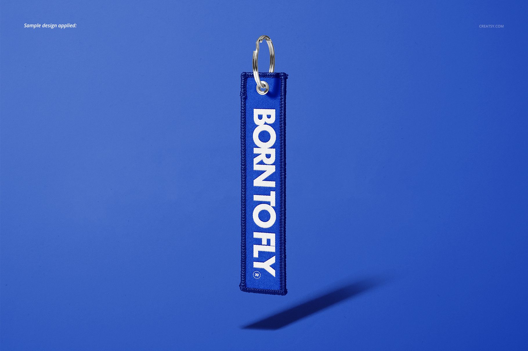 Front view of a blue Remove Before Flight keychain mockup with white lettering and a metal ring on a blue backdrop.