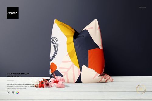 Decorative pillow mockup with vibrant geometric design, shown upright with floral props and dark background for presentation.