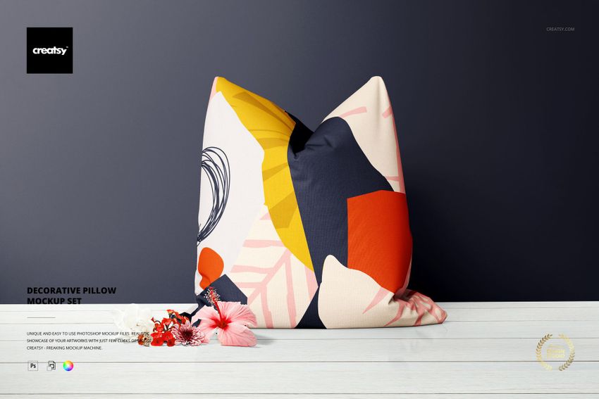 Decorative pillow mockup with vibrant geometric design, shown upright with floral props and dark background for presentation.