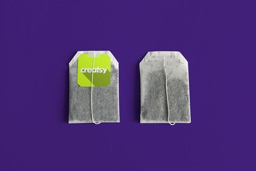 Tea bag mockup set showing two tea bags, one with a green label and one without, placed against a vibrant purple backdrop.