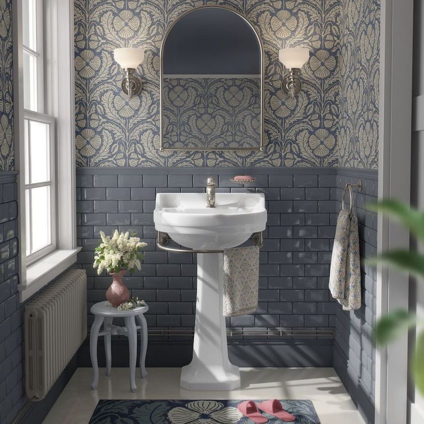 Vintage bathroom mockup with blue and beige floral wallpaper, pedestal sink, arched mirror, and wall sconces above tile walls.
