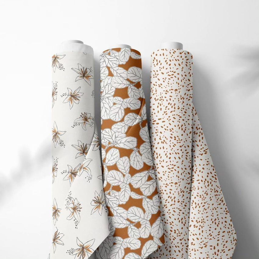 Fabric rolls mockup showing three upright rolls with different organic patterns in neutral and brown tones against a white background.