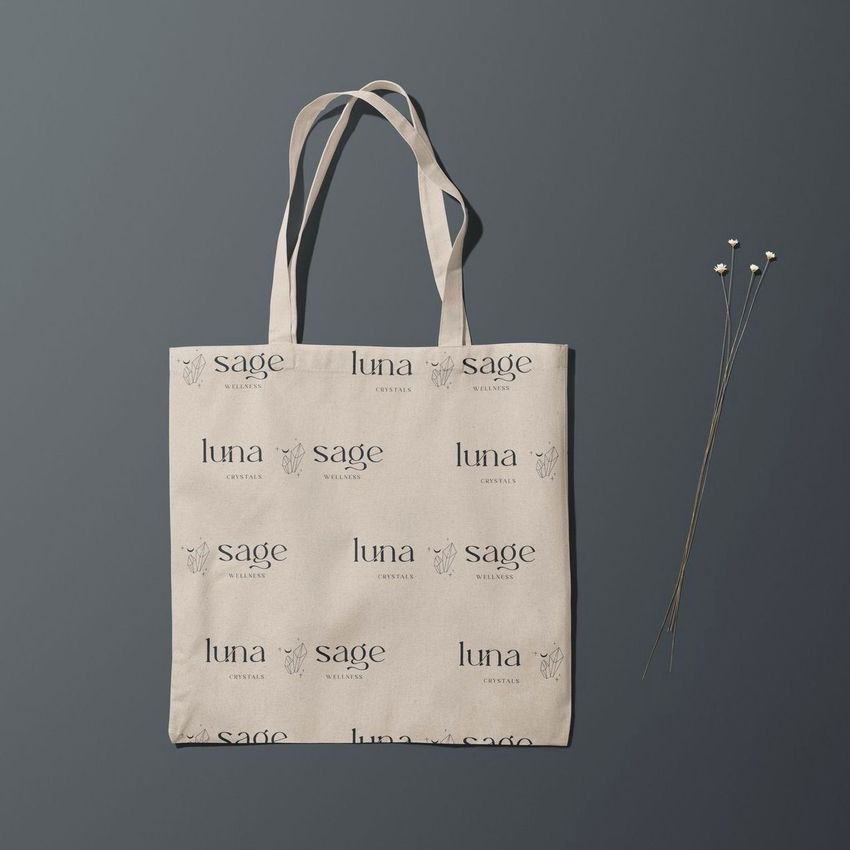 Tote bag mockup featuring a beige fabric bag with repeating black text and simple line art, placed on a gray surface with pins and stems.