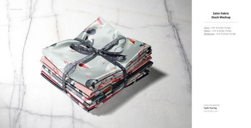 PSD mockup featuring a bundle of folded fabric swatches in assorted designs, arranged neatly with a black ribbon.