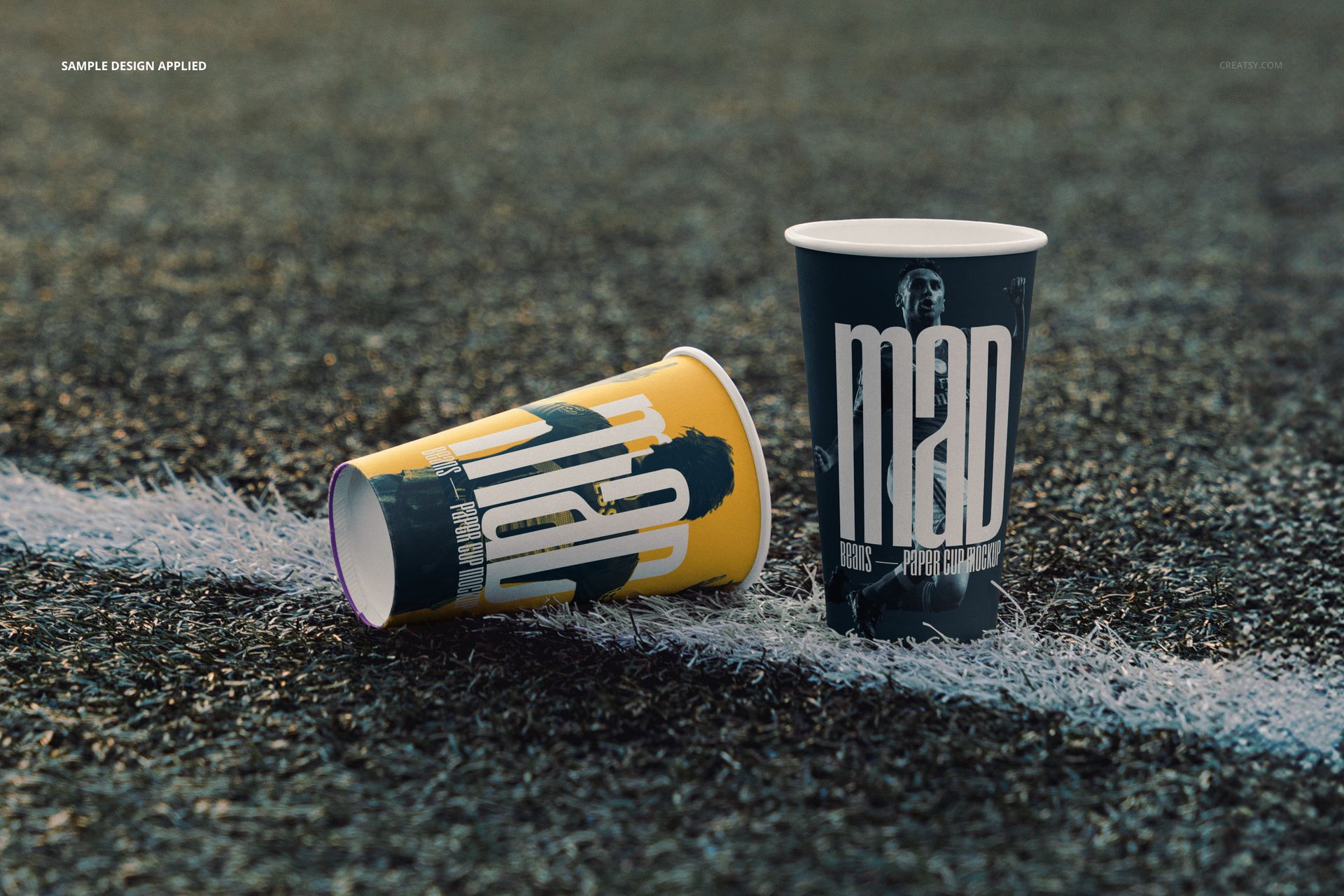 PSD mockup showing two decorated paper cups on an athletic field, with visible turf and white line markings.