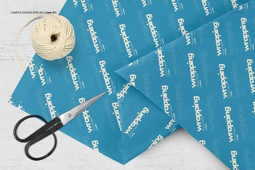 Wrapping tissue paper mockup featuring a blue sheet with white lettering, accompanied by scissors and a spool of twine.