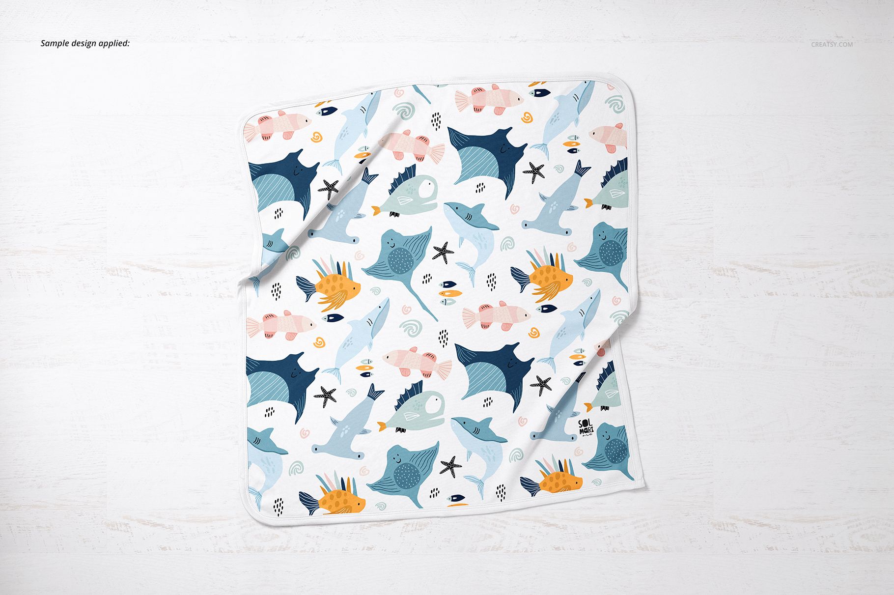 Square cotton baby blanket mockup featuring playful marine creatures in blue, orange, and pink, viewed from above.