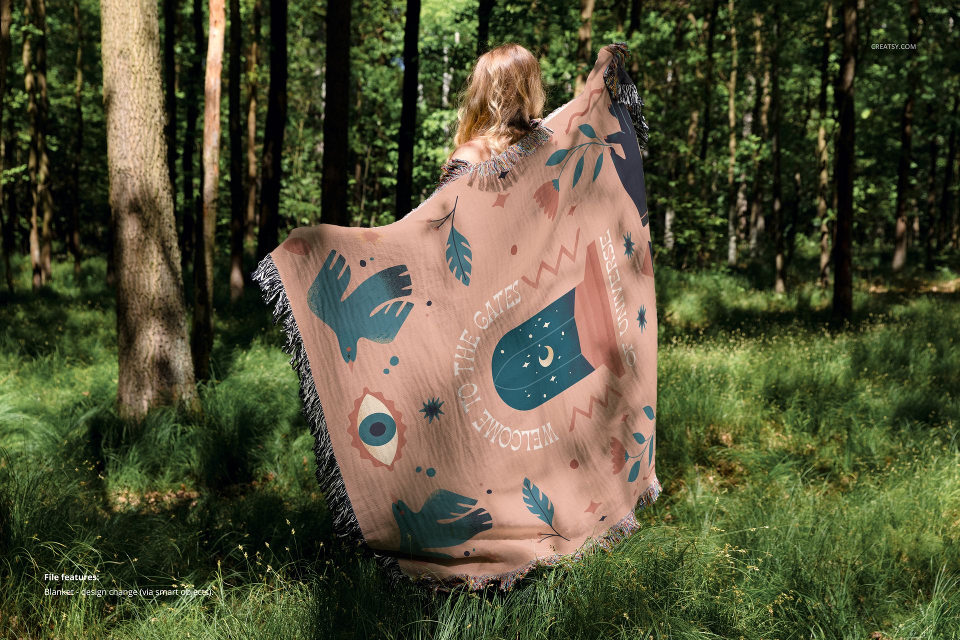 Mockup of a woven throw blanket with artistic design and fringes displayed outdoors among tall trees and grass.