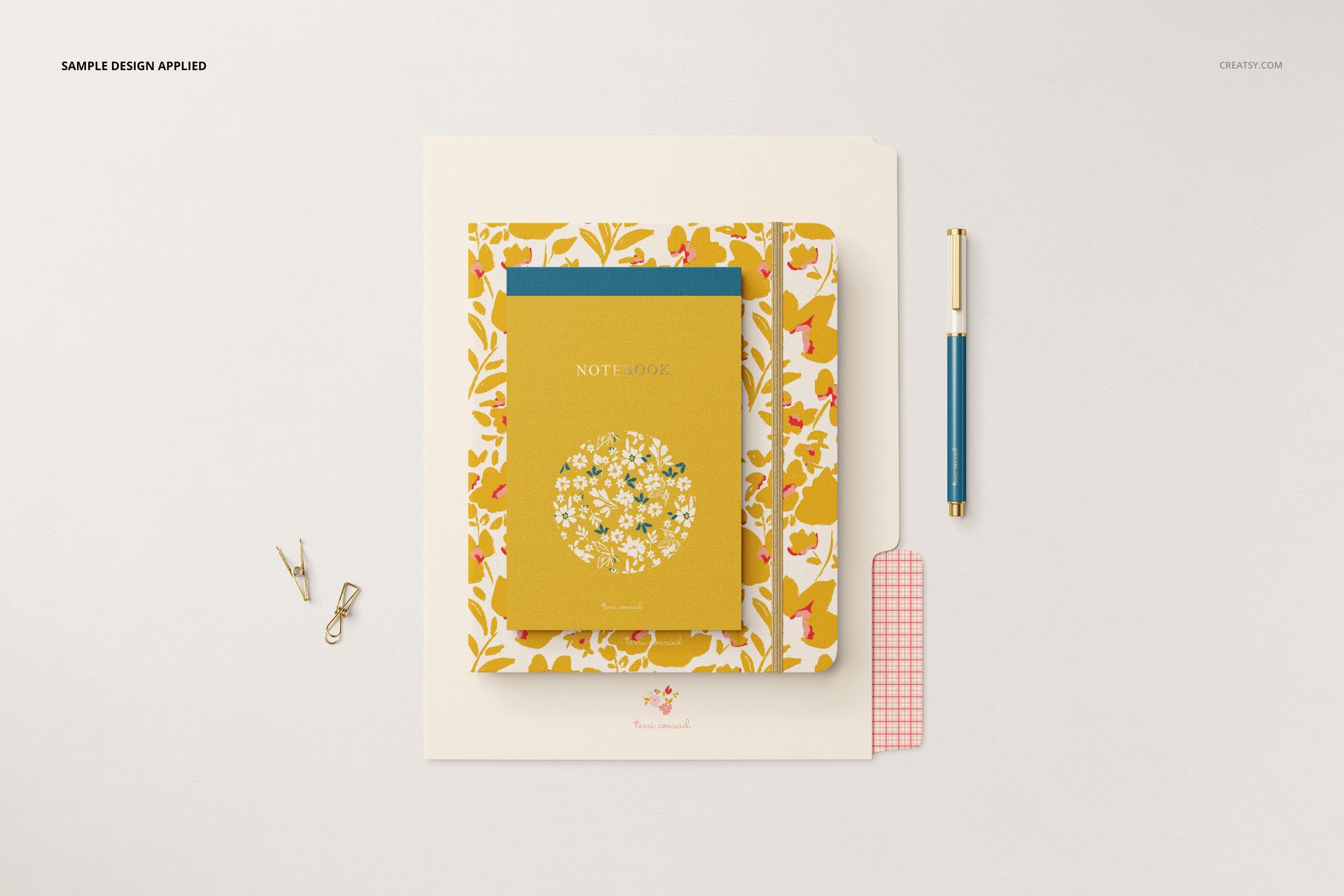 Stationery set mockup featuring a floral-patterned notebook, folder, pen, and paper clips arranged on a white surface.