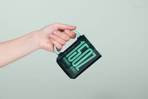 PSD mockup of a 15oz mug in black and mint green, held sideways by a hand with a minimalist backdrop.
