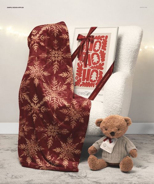 PSD mockup showing a red and gold patterned blanket, a decorative picture frame with ribbon, and a brown teddy bear in a cozy setting.