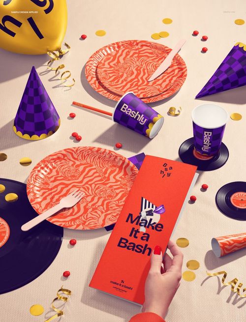 Disposable party tableware mockup featuring orange patterned plates, cups, and hats on a decorated tabletop.