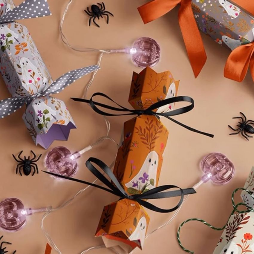 Halloween party cracker packaging mockup with illustrated ghost designs, ribbon ties, and decorative spiders on a peach background.