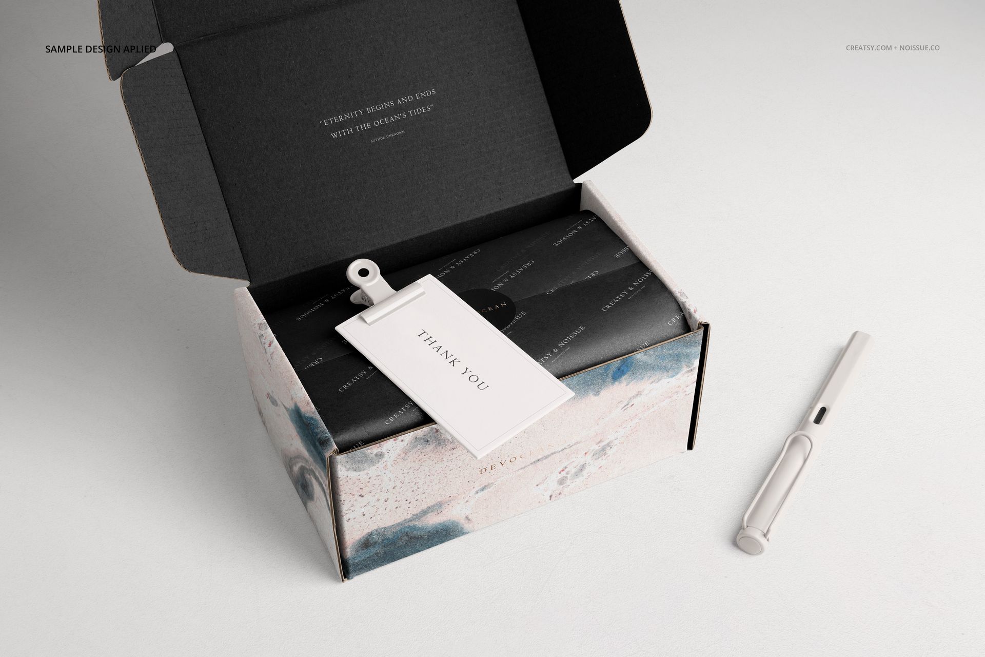 Front view of a packaging mockup showing an open mailing box with abstract design and a pen on a light surface.
