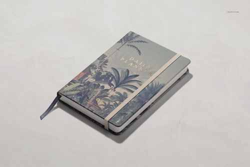 Front angled view of a leather notebook mockup featuring tropical leaf design and elastic closure on a pale background.