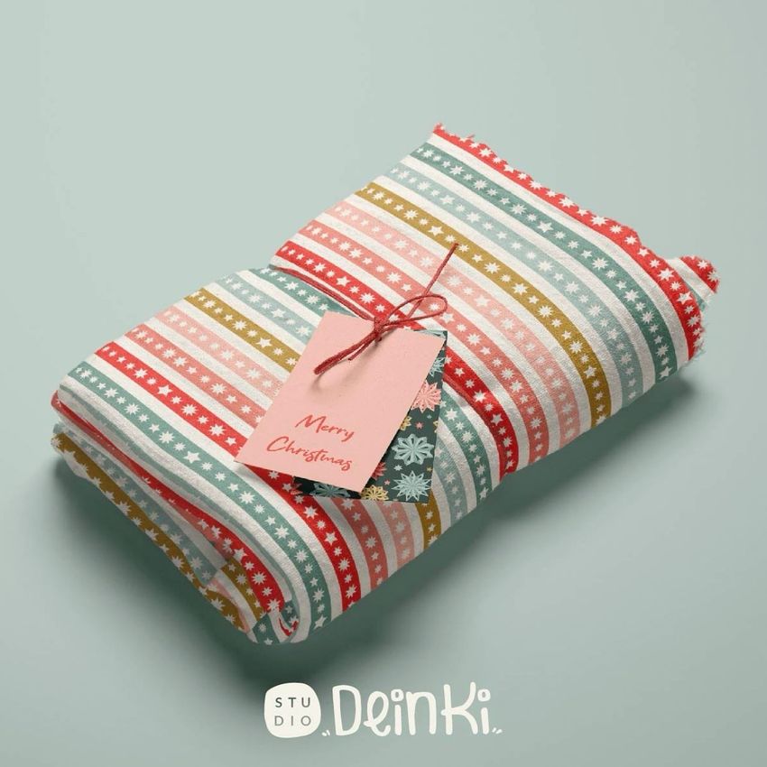 Muslin swaddle blanket mockup featuring a folded blanket with red, green, and white festive stripes and a gift tag on top.
