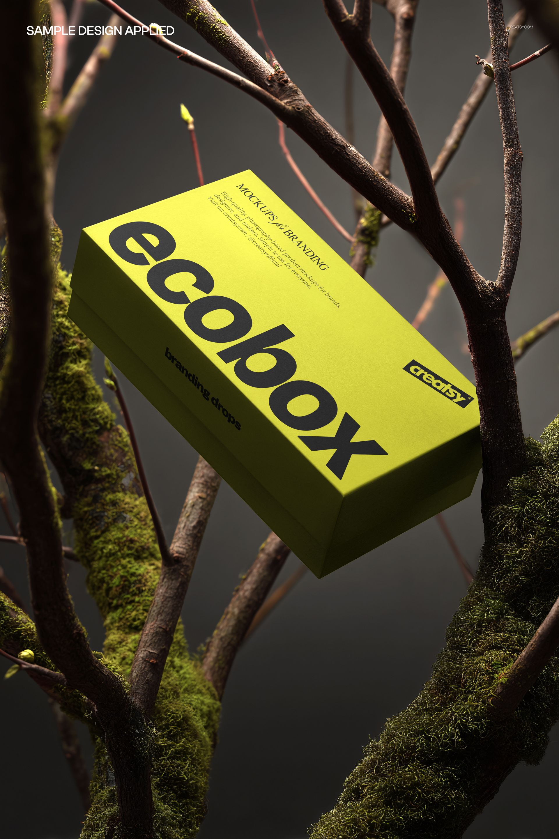 Green packaging box mockup with bold black lettering, positioned between natural branches covered in moss.
