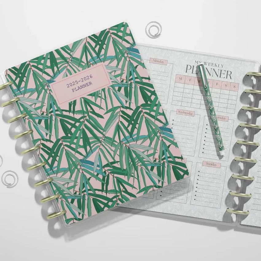 Top view of two spiral planners, one closed with a green bamboo leaf pattern on the cover, and one open showing a weekly planner layout.