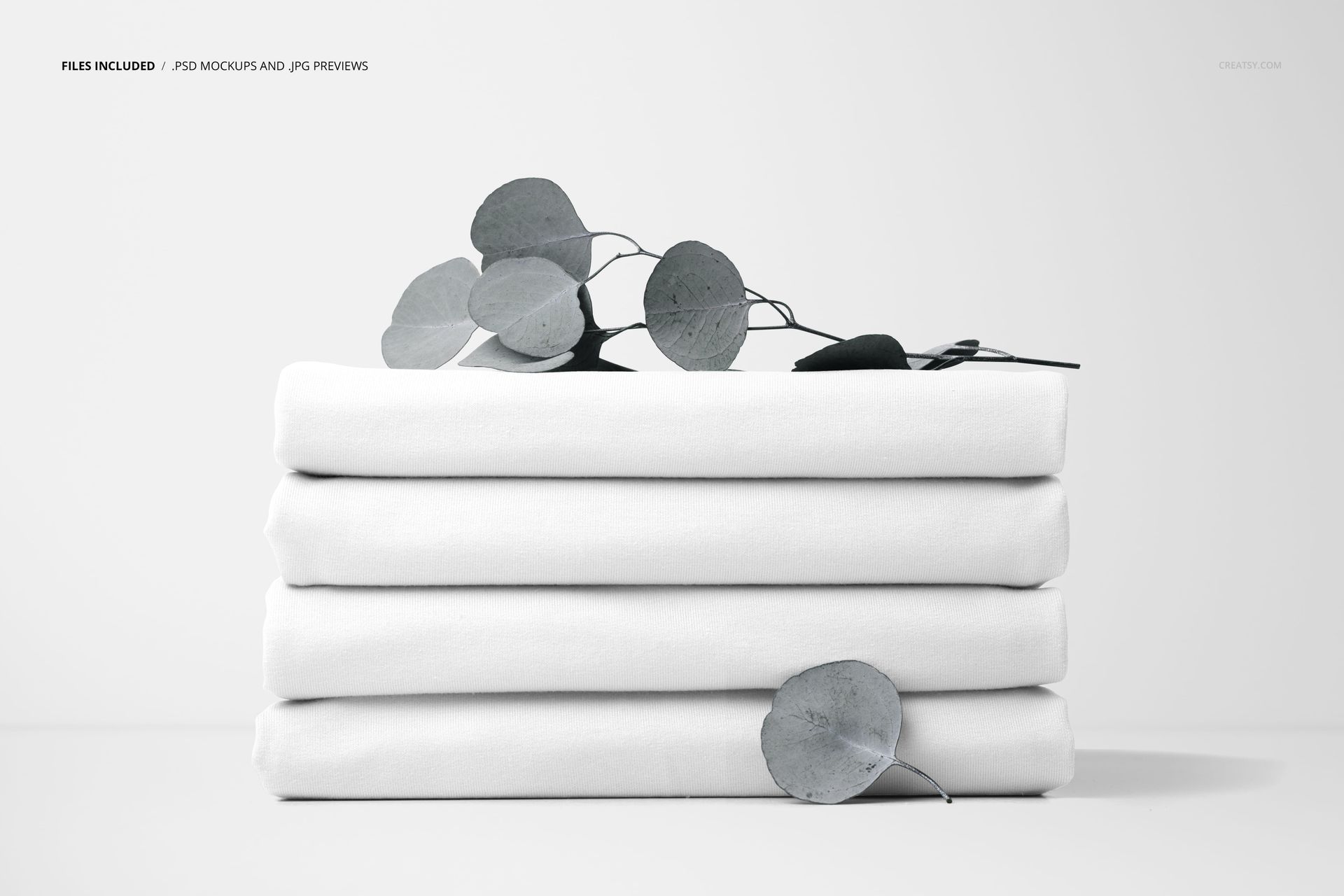 PSD mockup showing stacked white fabric pieces accented by eucalyptus leaves, photographed from a straight angle.