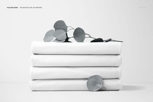 PSD mockup showing stacked white fabric pieces accented by eucalyptus leaves, photographed from a straight angle.