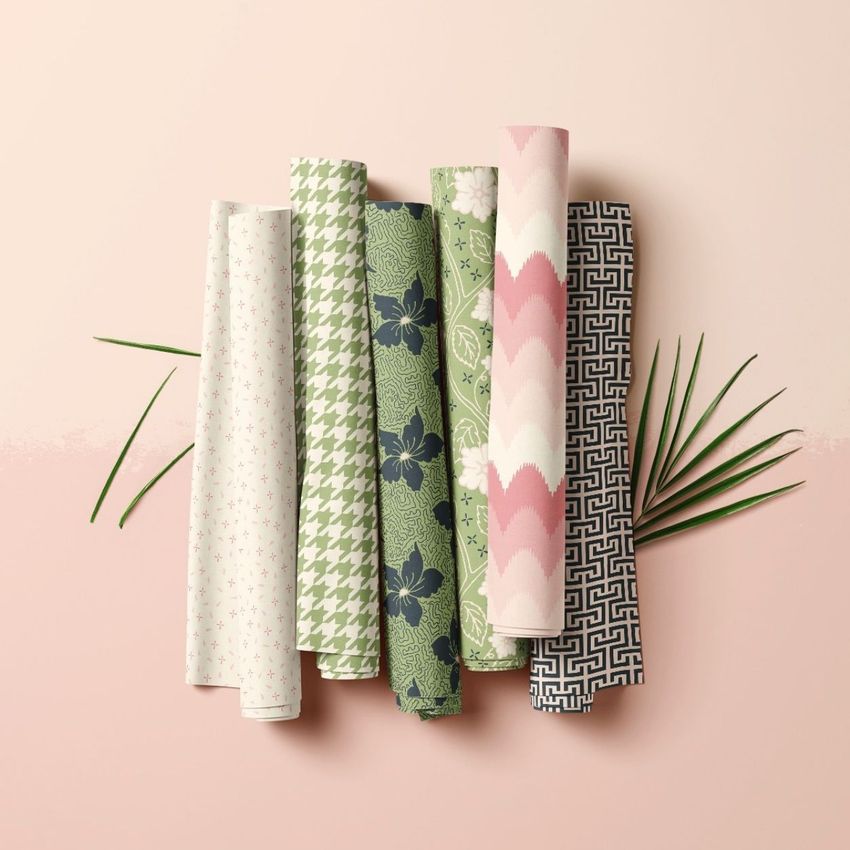 Fabric rolls mockup featuring six patterned fabric rolls in green, pink, and navy tones arranged on a light pink surface.