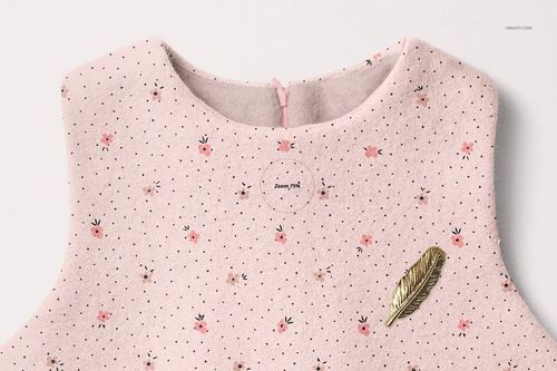 Front view of a baby dress mockup with a soft pink fabric, small floral pattern, and gold feather pin detail.