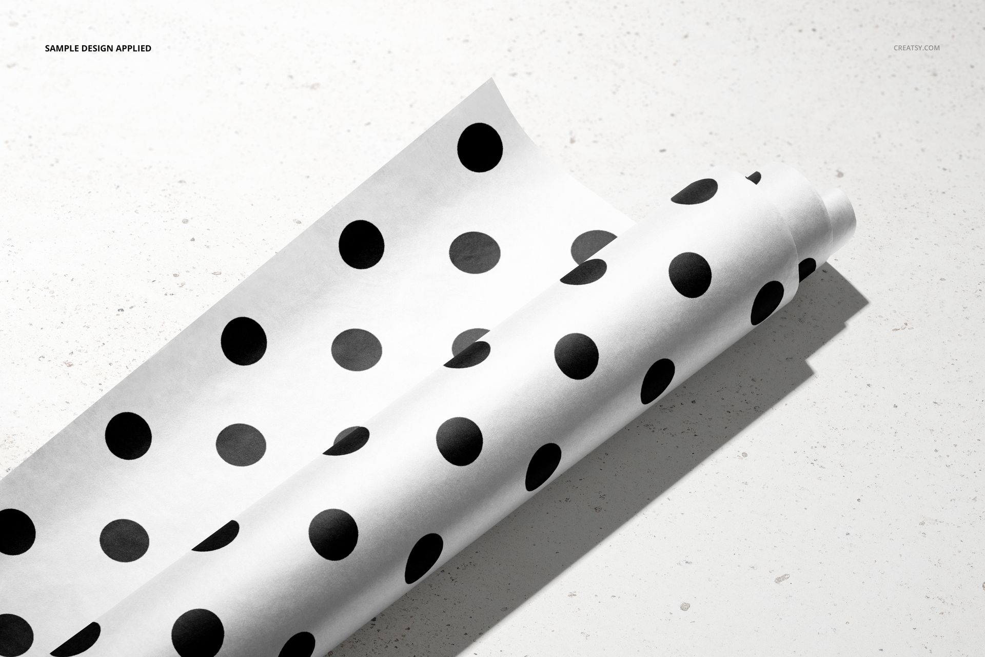 Front view of wrapping paper mockup featuring large black dots on white, placed on a neutral stone background.