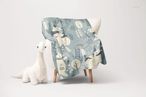 Fleece blanket with rounded corners draped over a sherpa chair, featuring a playful polar bear pattern in soft blue tones.