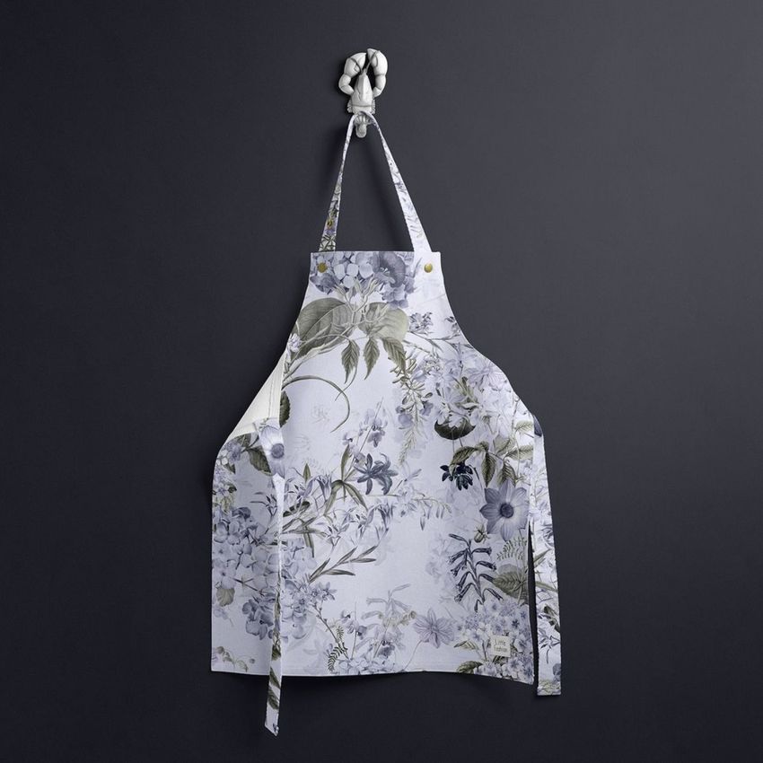 Kids apron mockup featuring a white apron with a delicate blue and green floral pattern, hanging on a dark gray wall.