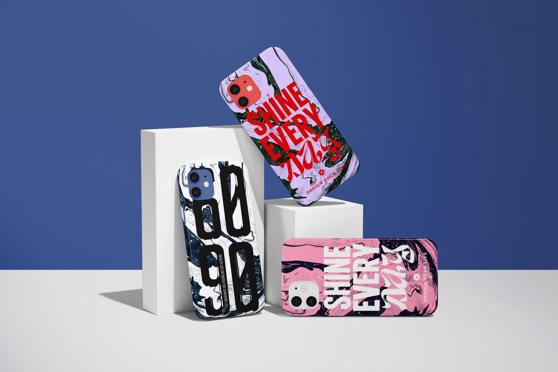 PSD mockup showing three iPhone 12 cases in assorted colors and graphic prints, positioned upright on minimalist white props.