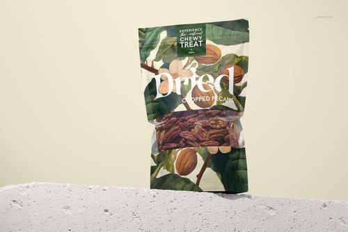 Standing paper pouch mockup with chopped pecans visible through a clear window, leafy design and beige backdrop.
