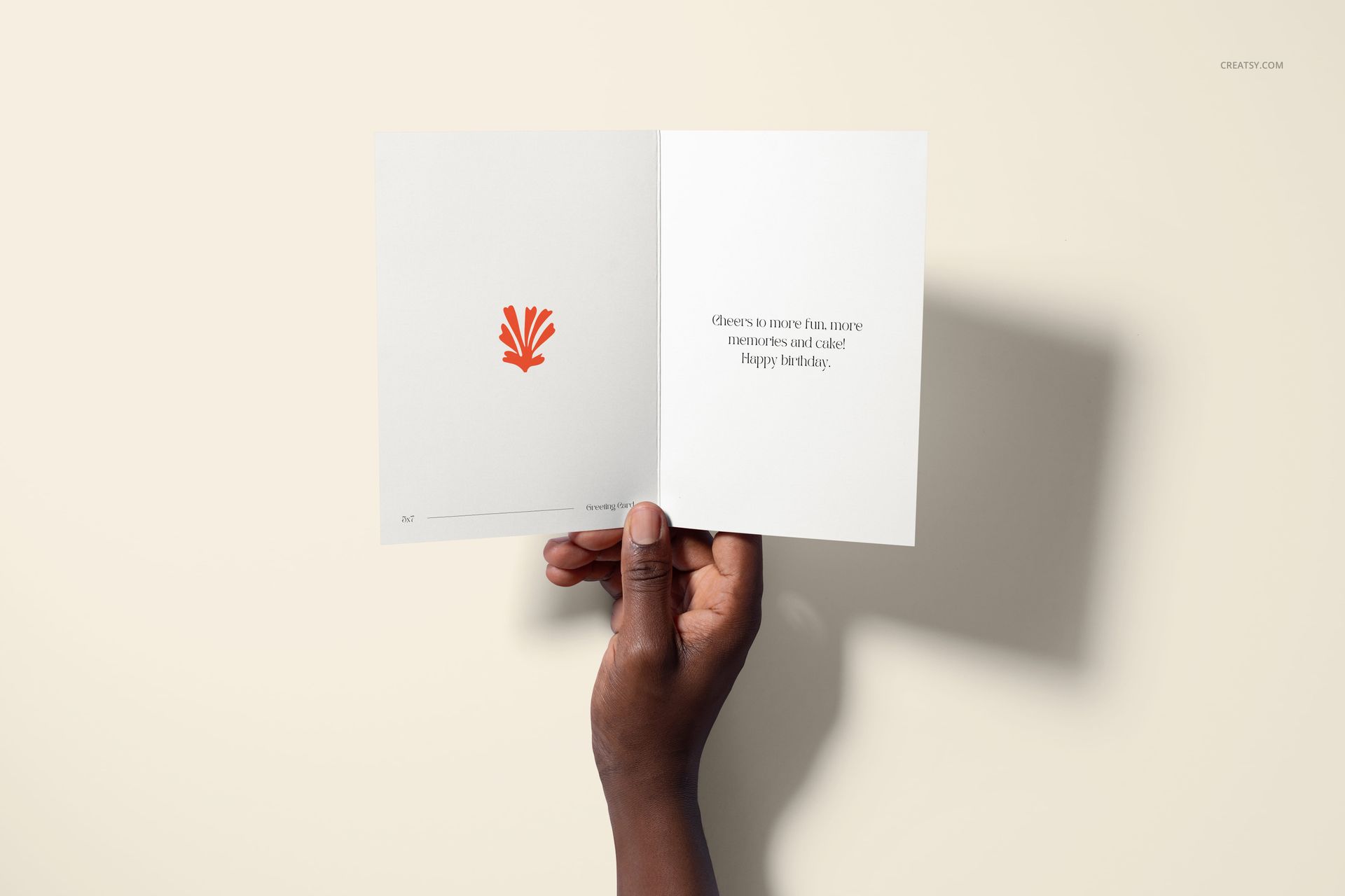 Open greeting card mockup with white interior, orange abstract illustration, and birthday message held by a hand.