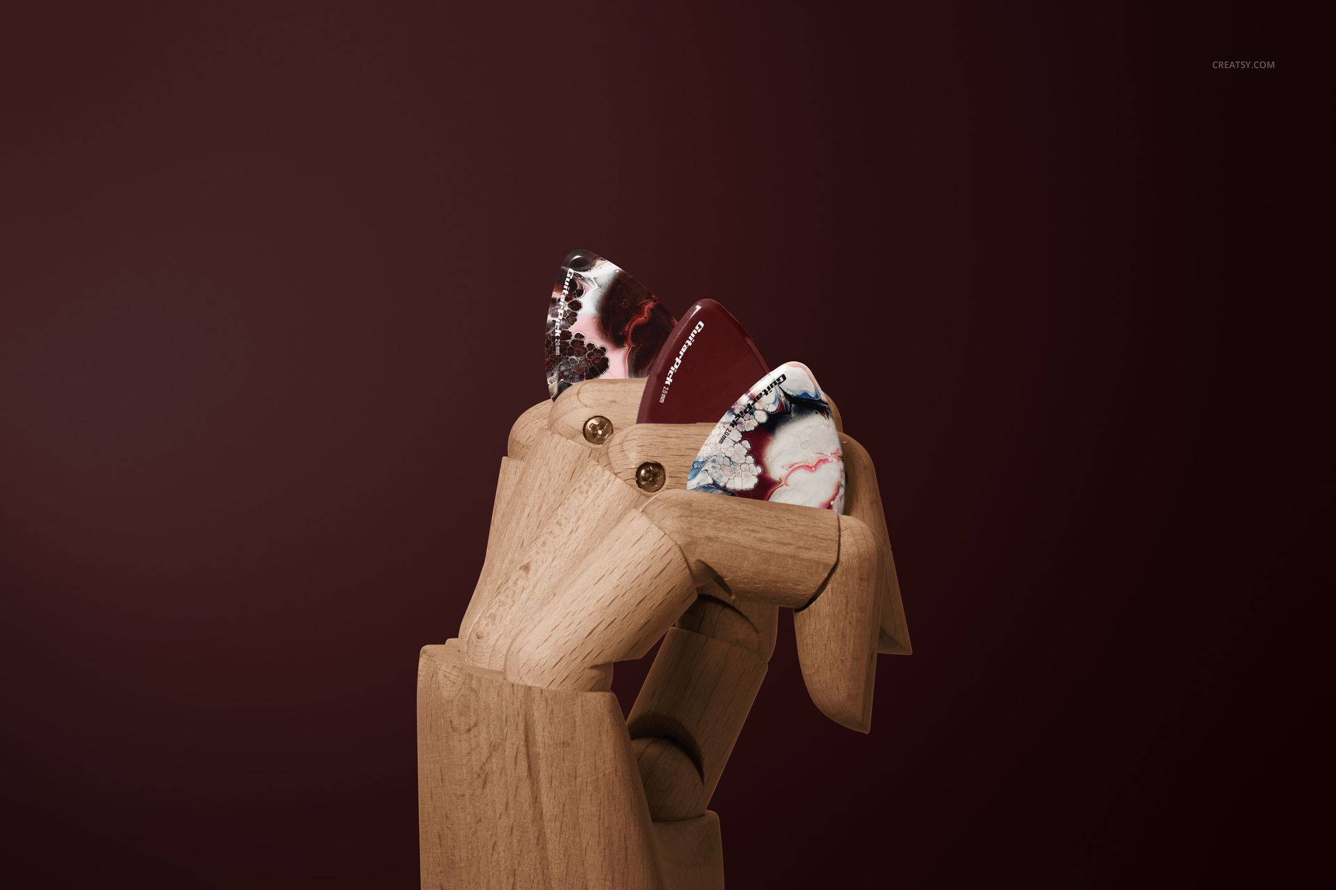 PSD mockup featuring a wooden hand displaying three multi-colored guitar picks, set before a solid burgundy background.