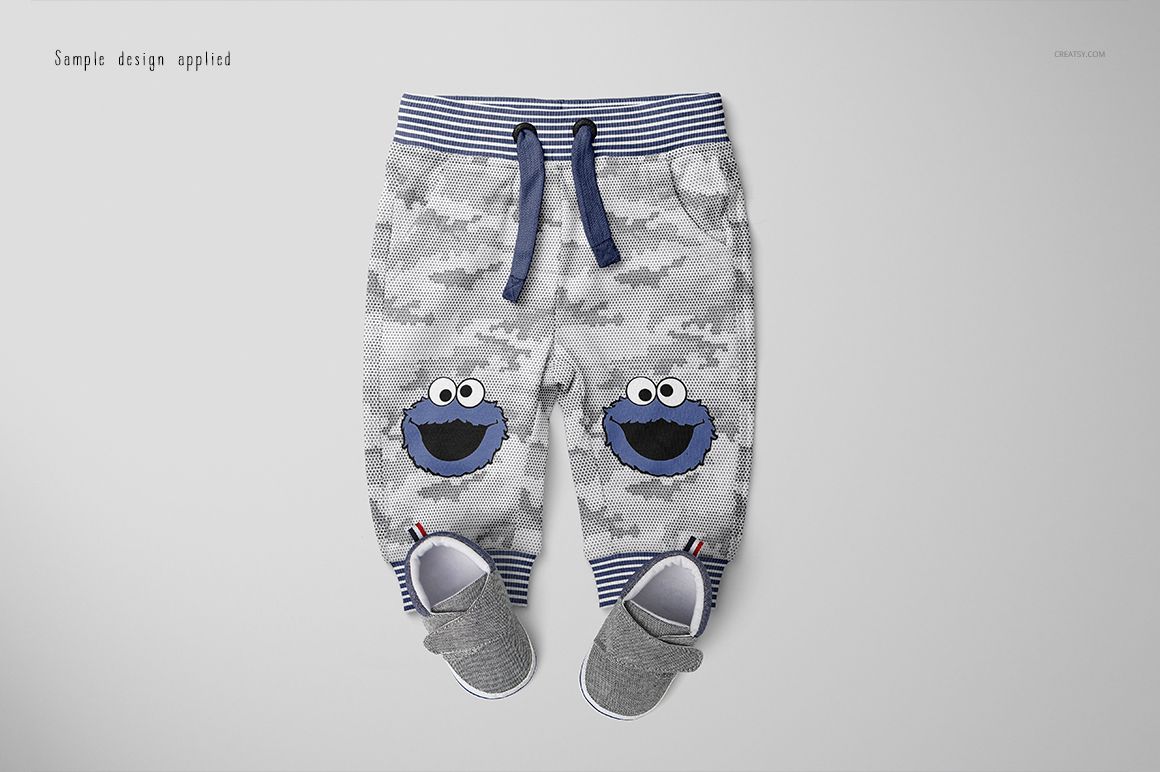 Front view of baby sweatpants mockup with gray camouflage pattern, blue waistband, and cartoon faces on knees.