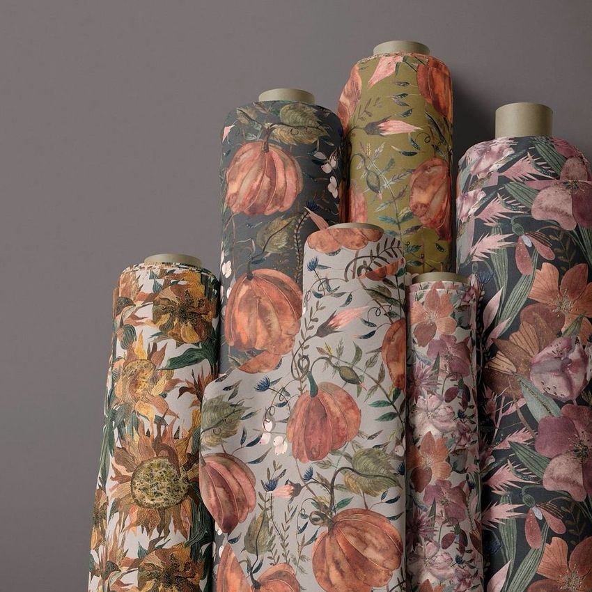 Fabric rolls mockup featuring seven upright rolls with autumn-inspired floral and pumpkin patterns against a neutral wall.
