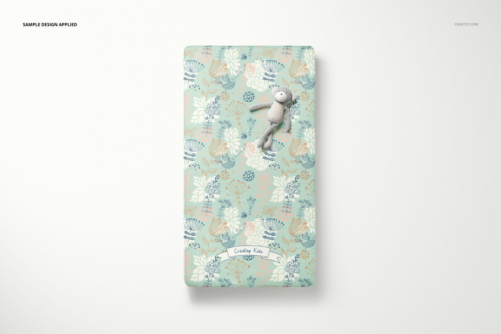 Crib sheet mockup displaying a botanical print in soft blue and beige tones, with a stuffed toy on top.