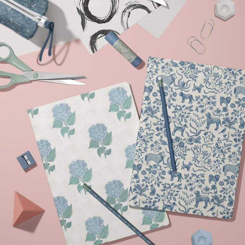Stationery mockup featuring two classic A4 notebooks with floral and animal patterns, pencils, scissors, and paper clips on a pink surface.