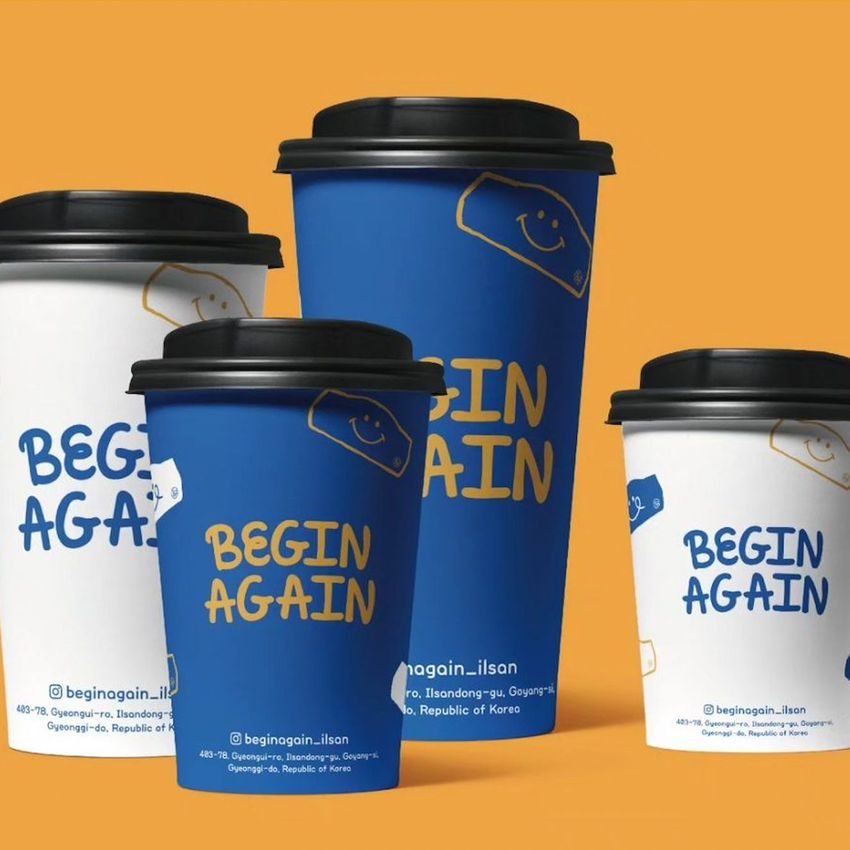 Paper cups mockup featuring four cups with black lids, two in blue and two in white, arranged on an orange background.
