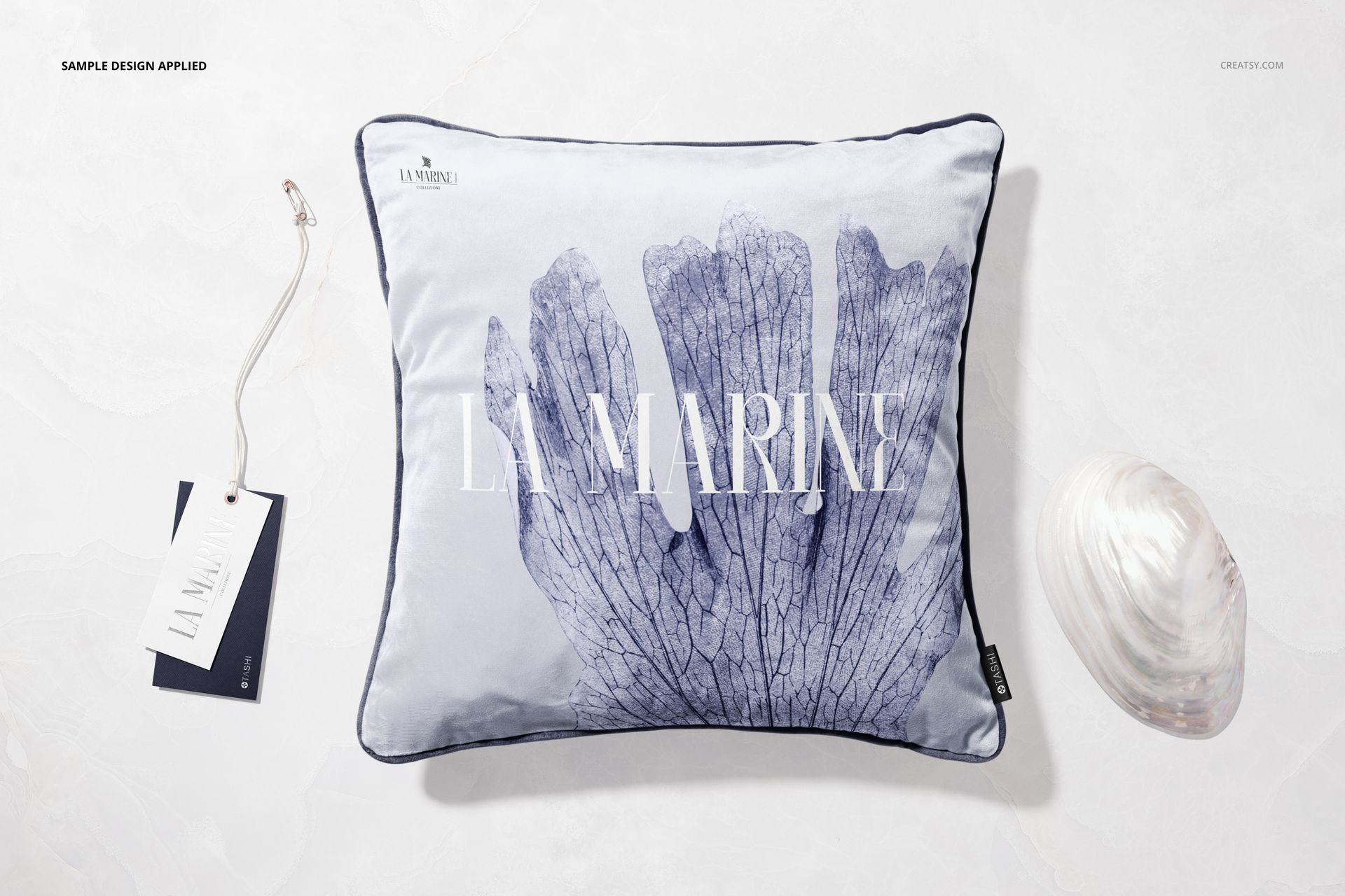 Front view of a square velvet cushion mockup with blue leaf pattern, dark edging, and a shell placed beside it.