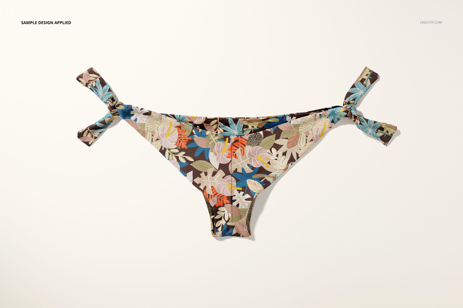 Bikini bottom mockup with knotted sides, displaying a vibrant leaf and flower print on a light surface.